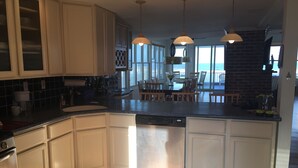 A modern kitchen with white cabinetry, a dishwasher, and a dining area with wooden chairs. - LBI Oceanfront. Beautiful! Views galore. Dine overlooking the dunes. (Beach Haven Crest)