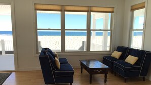 A living room with a wooden floor, a blue sofa, a matching armchair, and a coffee table. Large windows provide a view of the beach and ocean. - LBI Oceanfront. Beautiful! Views galore. Dine overlooking the dunes. (Beach Haven Crest)