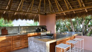 A modern kitchen with a large island, wooden cabinets, and a thatched roof. - Casita Mimas: High design, great views, romantic retreat  (Sayulita)
