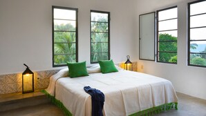 A bedroom with a bed, two windows, and a nightstand with a lamp. - Casita Mimas: High design, great views, romantic retreat  (Sayulita)