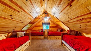 Un dormitorio acogedor en el ático con dos camas, una ventana y un ventilador de techo.