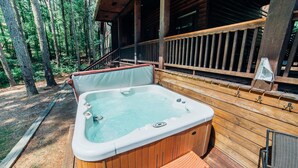 Un jacuzzi en una terraza de madera con barandilla y vista a árboles.