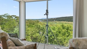 A room with large windows offering a view of a green landscape and a tripod in the center. - Panoramic Views (Aireys Inlet)