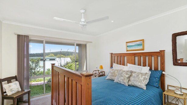 A bedroom with a bed, a nightstand, a chair, a window with curtains, a ceiling fan, and a painting on the wall. - Panoramic Views (Aireys Inlet)