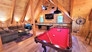 Ein gemütlicher Raum mit Holzboden, einer Billardkugel, einem Sofa, einem Fernseher und einem Dartboard.