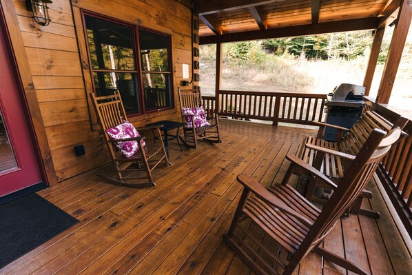 A wooden deck with rocking chairs and a grill.