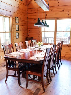 A wooden dining room with a large table set for six, surrounded by chairs.