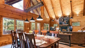 A wooden cabin interior with a dining area, kitchen, and fireplace. - Rock Hollow Cabin - Built For Quality! (Rockbridge)