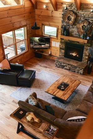 Un acogedor interior de cabaña con chimenea de piedra, asientos de cuero y televisión.