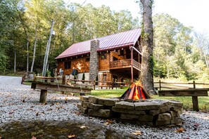A log cabin with a stone fireplace, wooden deck, and a metal roof.