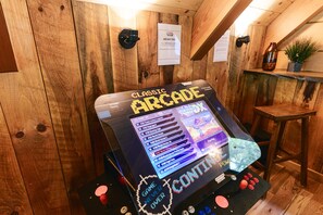 Une borne d’arcade classique dotée d’un écran numérique, entourée de murs en bois et agrémentée d’une petite table sur laquelle est posée une plante.