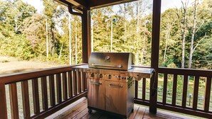 Ein tragbarer Grill auf einer Holzterrasse mit Blick auf einen Wald.
