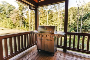 Ein tragbarer Grill auf einer Holzterrasse mit Blick auf einen Wald.