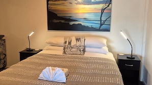 A neatly made bed with a printed pillow, two bedside tables with lamps, and a large painting of a sunset over the sea on the wall. - G SPOT lower level WITH SPA (Raglan)