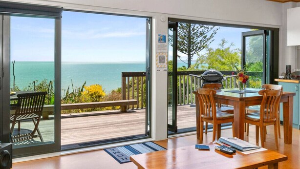 A room with a wooden table and chairs, a grill, and a view of the ocean. - G SPOT lower level WITH SPA (Raglan)