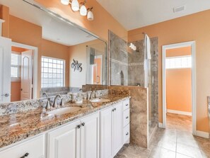 A modern bathroom with a granite countertop, a glass shower enclosure, and a large mirror. - Sea Turtle Tango- Close to beach! Community Pool! (Galveston)