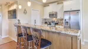 Una cocina con encimera de granito, electrodomésticos de acero inoxidable y taburetes de bar.