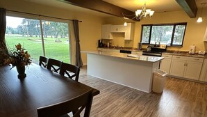 Eine moderne Küche mit einer großen Kochinsel, einem Essbereich mit Holztisch und Stühlen sowie Blick auf einen Golfplatz durch die Fenster.