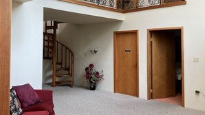 Ein großzügiger Wohnbereich mit einem roten Sofa, einer Treppe und einem Balkon mit dekorativen Geländern.
