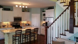 A kitchen with a central island, white cabinets, a microwave, and a refrigerator. - Bay Point Experience (Marblehead)