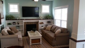 A living room with a fireplace, two sofas, a coffee table, and a TV mounted above the fireplace. - Bay Point Experience (Marblehead)