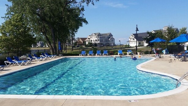 A rectangular swimming pool with clear blue water, surrounded by lounge chairs and umbrellas, with houses in the background. - Bay Point Experience (Marblehead)