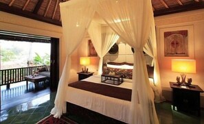 A four-poster bed with white drapes, a nightstand with a lamp, and a view of the outdoors. - 2 Bedroom villa in Canggu Beachfront property. (Canggu)