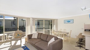 Un vaste espace de vie comprenant un canapé, une table à manger et des chaises. De grandes fenêtres laissent entrer beaucoup de lumière naturelle et offrent une vue sur l’extérieur.