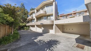 Un immeuble résidentiel moderne à plusieurs étages, doté d’un balcon incurvé, d’un garage et d’une allée bien entretenue.