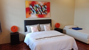 Ein Schlafzimmer mit einem großen Bett, einem kleineren Bett, einem Wandbild und zwei Nachttischen mit Lampen.