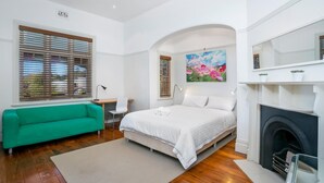 Ein modernes Schlafzimmer mit Bett, einem grünen Sofa, einem Schreibtisch und einem Kamin.