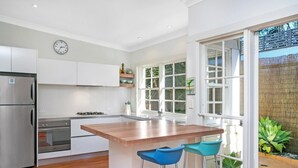 Eine moderne Küche mit weißen Schränken, einem Edelstahlkühlschrank, einem Gasherd und einer Holztheke mit zwei Barhocker.