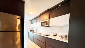 Una cocina moderna con armarios oscuros, un refrigerador de acero inoxidable, un microondas y un salpicadero de azulejos.