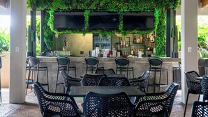 Un área de bar al aire libre con una pared cubierta de plantas verdes, una barra y sillas de mimbre negro.