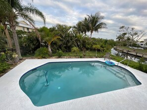 Una piscina de borde curvo, rodeada de palmeras y un área con césped.