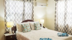 A hotel room with a bed, two bedside lamps, a nightstand, and patterned curtains. - Comfortable beachfront cottage, full amenities, fabulous deck overlooking beach  (St. Peter)