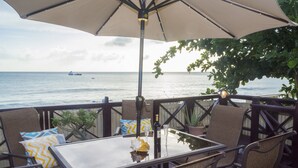 An outdoor patio with a table and chairs, overlooking the sea. - Comfortable beachfront cottage, full amenities, fabulous deck overlooking beach  (St. Peter)