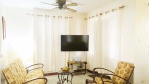 A living room with two rocking chairs, a flat-screen TV, and a ceiling fan. - Comfortable beachfront cottage, full amenities, fabulous deck overlooking beach  (St. Peter)