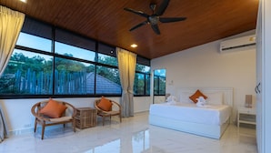 Une chambre à coucher moderne avec un grand lit, deux fauteuils en osier, une petite table et un ventilateur de plafond.