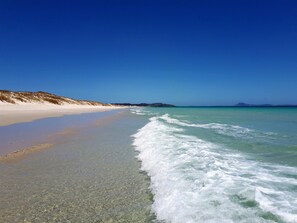 A beach with clear turquoise water, a sandy shore, and distant hills. - Relax in Rangiputa - Decks, Beaches and Boating (Rangiputa Beach)