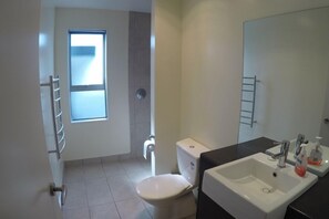 A modern bathroom with a toilet, sink, and mirror. - Relax in Rangiputa - Decks, Beaches and Boating (Rangiputa Beach)