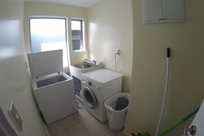 A compact laundry area with a washing machine, dryer, and a small trash bin. - Relax in Rangiputa - Decks, Beaches and Boating (Rangiputa Beach)