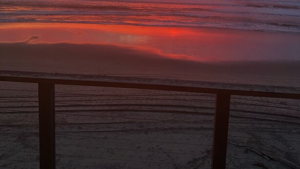 Ein Sonnenuntergang über dem Meer mit einem hölzernen Deck im Vordergrund.