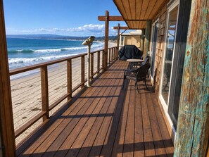 A wooden deck with a view of the beach, a telescope, and outdoor seating.