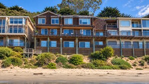 Ein Strandhotel mit mehreren Balkonen, einer Holzfassade und einem Sandstrand im Vordergrund.