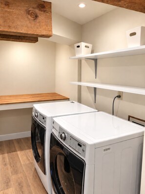 A laundry room with two washing machines, wooden shelves, and a wooden bench. - Beach Front Vacation Rental-The Beach is your back yard - Santa Cruz (Watsonville)