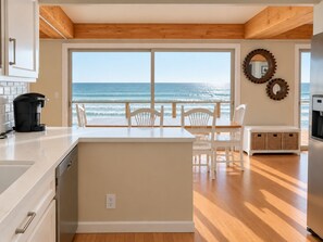 A kitchen with a view of the ocean, wooden flooring, and a white island with seating.