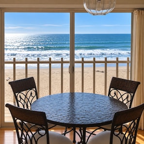 Une table ronde avec quatre chaises, une vue sur la plage et une balustrade de balcon.
