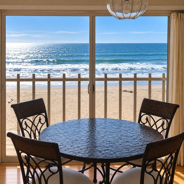A round table with four chairs, a view of the beach, and a balcony railing.