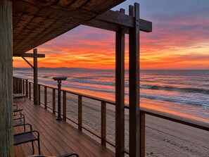 Una terraza de madera con vista a una playa y al atardecer.